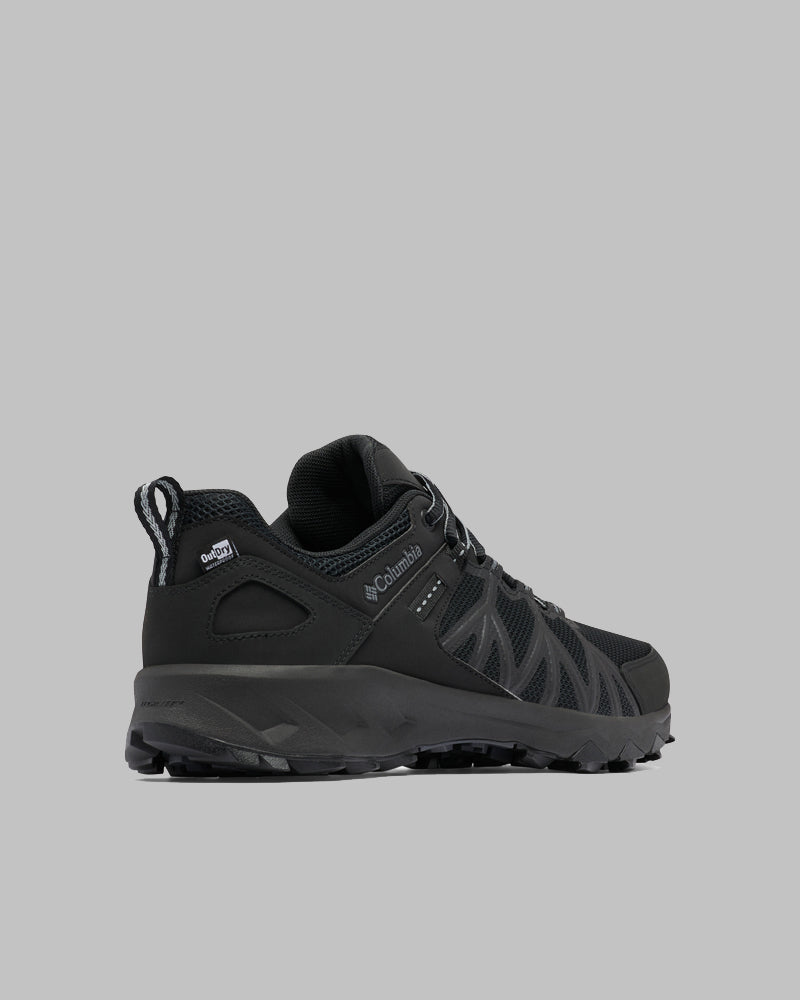 נעלי טיולים שחורות מדגם Peakfreak II Outdry של ColumbiaIL, עם סוליה מחוספסת, רשת וחיפויים סינתטיים, ולוגו Outdry, מוצגות על רקע אפור אחיד, בזווית המציגה את הצד והחלק האחורי.