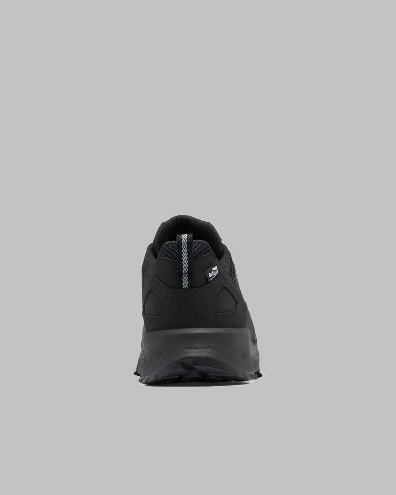 נעלי הטיולים "Peakfreak II Outdry" של ColumbiaIL בצבע שחור מוצגות במבט מאחור על רקע אפור אחיד, תוך הדגשת העקב, הסוליה המרקמת ולשונית הבד עם הלוגו הבולט — אידיאליות לחובבי פעילויות בחיק הטבע.