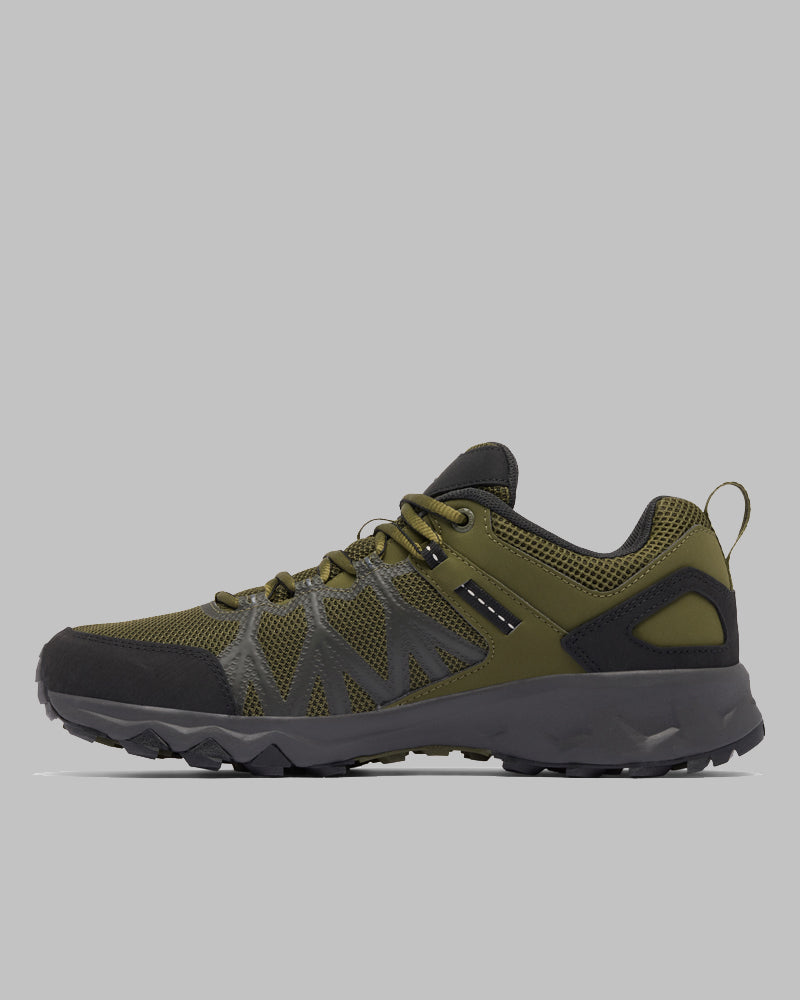 מבט צדדי על נעל הטיולים ColumbiaIL Peakfreak II Outdry בצבעי ירוק זית ושחור, עם סוליה מחוספסת, חלק עליון מרשת, שרוכים ולשונית משיכה בעקב, על רקע אפור בהיר.