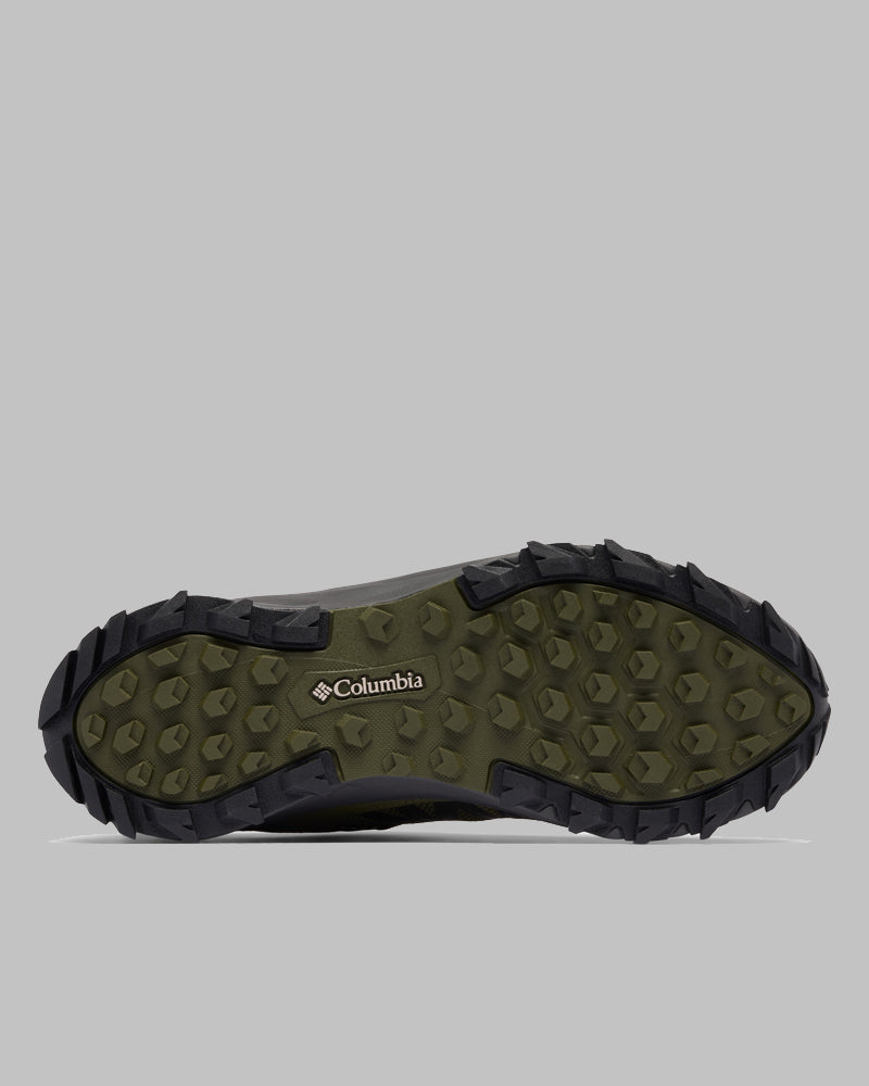 מבט מלמטה על נעל Columbia Peakfreak II Outdry עם סוליה ירוקה ודפוס שחור מחוספס לאחיזה, המוצגת על רקע אפור אחיד.