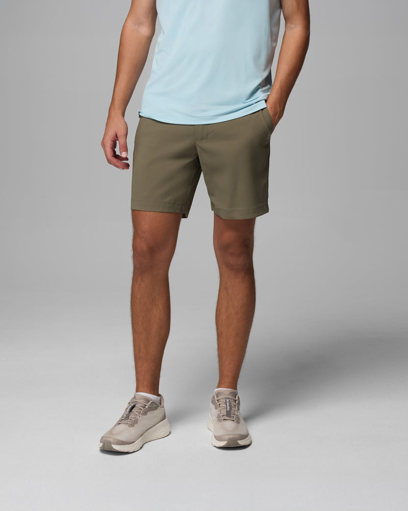 אדם לבוש בחולצה תכלת, מכנסיים קצרים מדגם "Tech Trail Utility Short" של קולומביה ישראל בצבע ירוק זית, ונעלי ספורט בצבע בז', עומד כש יד אחת בכיס על רקע אפור אחיד. ראשו אינו נראה.