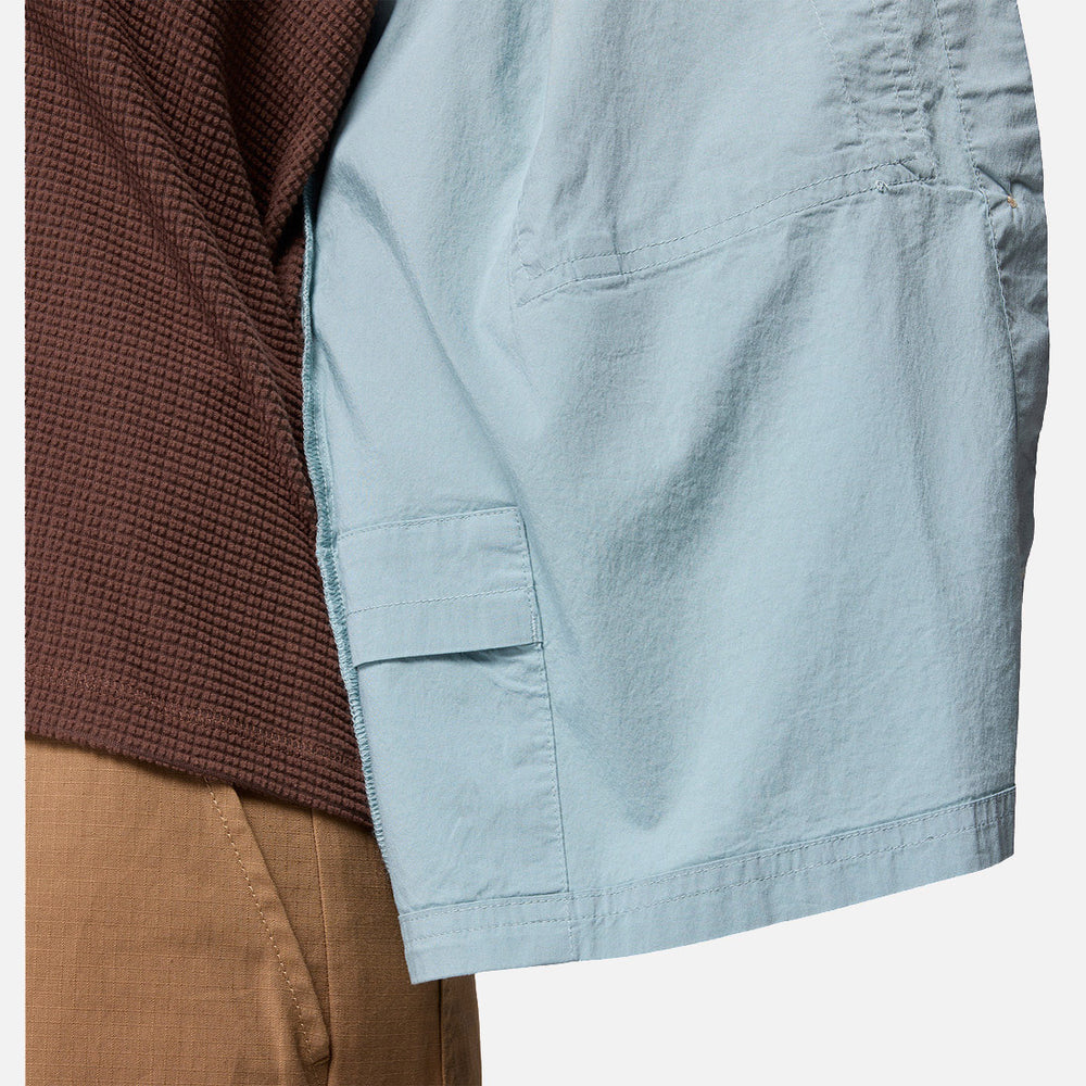תקריב של אדם הלובש את חולצת "Brea Falls Woven Long Sleeve Shirt" של קולומביה ישראל בצבע תכלת כחול כמעיל עליון, בשילוב עם מכנסיים בצבע חום בהיר. נראים רק פלג הגוף העליון וחלק מהזרוע.