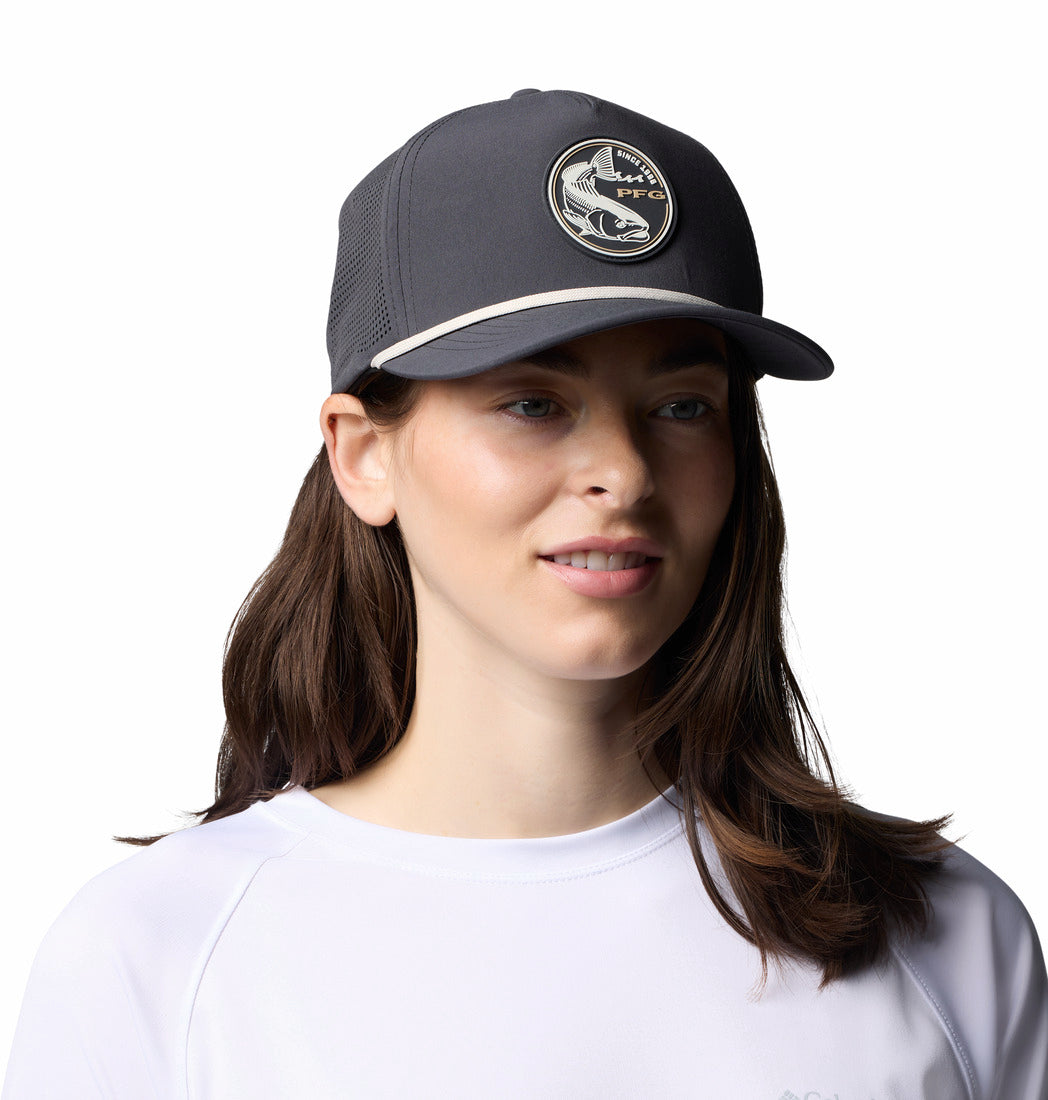 אישה בעלת שיער חום ארוך, החובשת כובע "ColumbiaIL Tidal Pursuit 3d Stretch Snap Back" בצבע אפור כהה עם לוגו של דג עגול, ולובשת חולצה לבנה, מחייכת ברכות תוך שהיא מביטה לצד, על רקע לבן חלק.