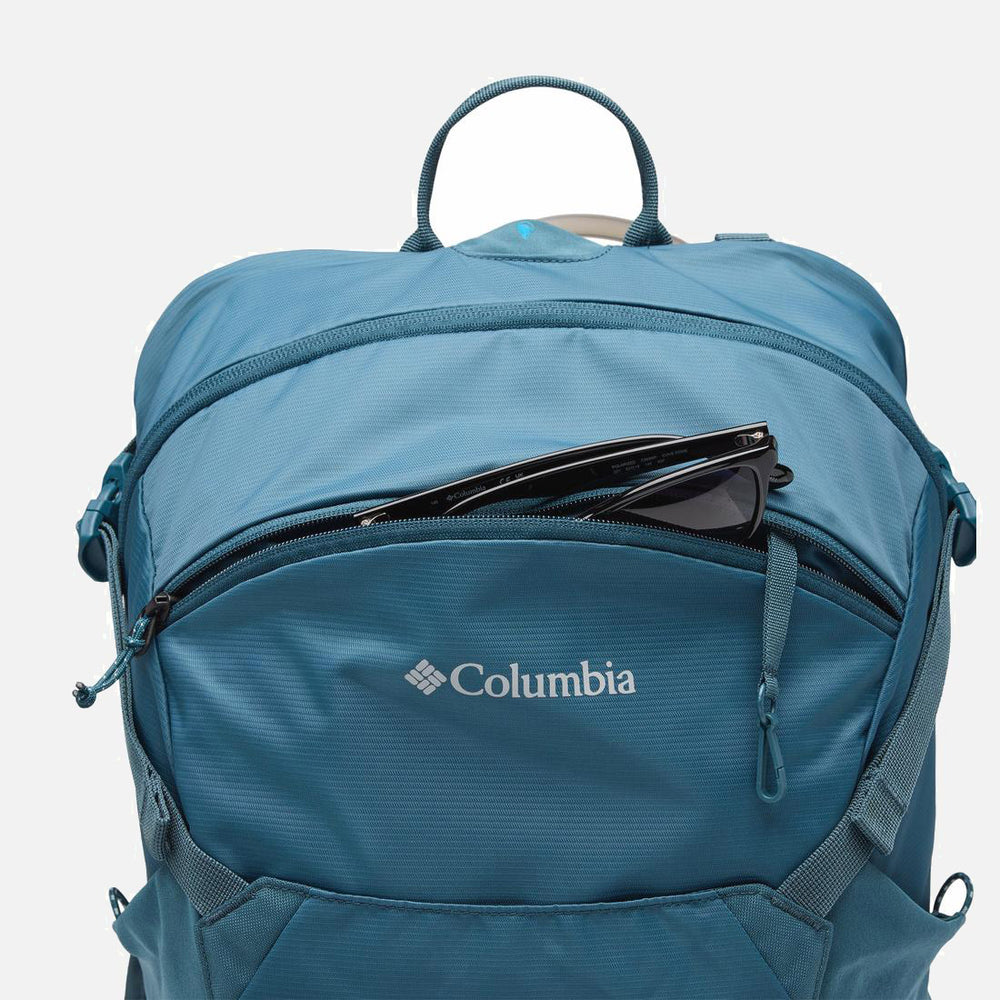 תיק הגב "Blackcomb Ridge 30L" של המותג ColumbiaIL בצבע כחול מוצג על רקע לבן חלק, כשמשקפי שמש שחורים תחובים חלקית בכיס הקדמי עם הרוכסן.