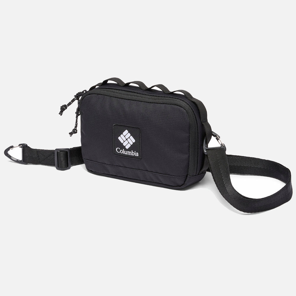 תיק הצלב "Trail Traveler" של ColumbiaIL הוא תיק שחור קטן עם רצועה מתכווננת, שני תאים עם רוכסן ולוגו המותג בחזית, המוצג על רקע לבן חלק.