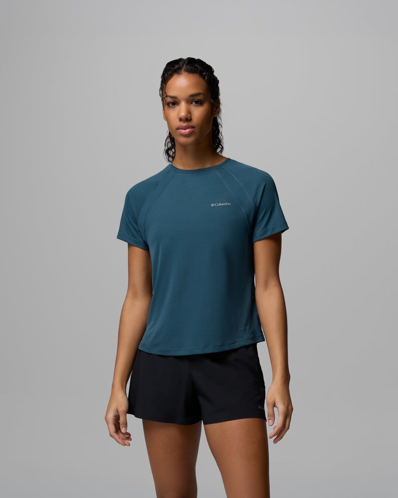 על רקע אפור אחיד, אדם לבוש בחולצת ה-Stealth Spring Short Sleeve Tee של קולומביה ישראל בצבע טיל ובמכנסיים קצרים שחורים, מביט למצלמה במבט ניטרלי — אווירה מושלמת של קולקציית STEALTH SPRING.
