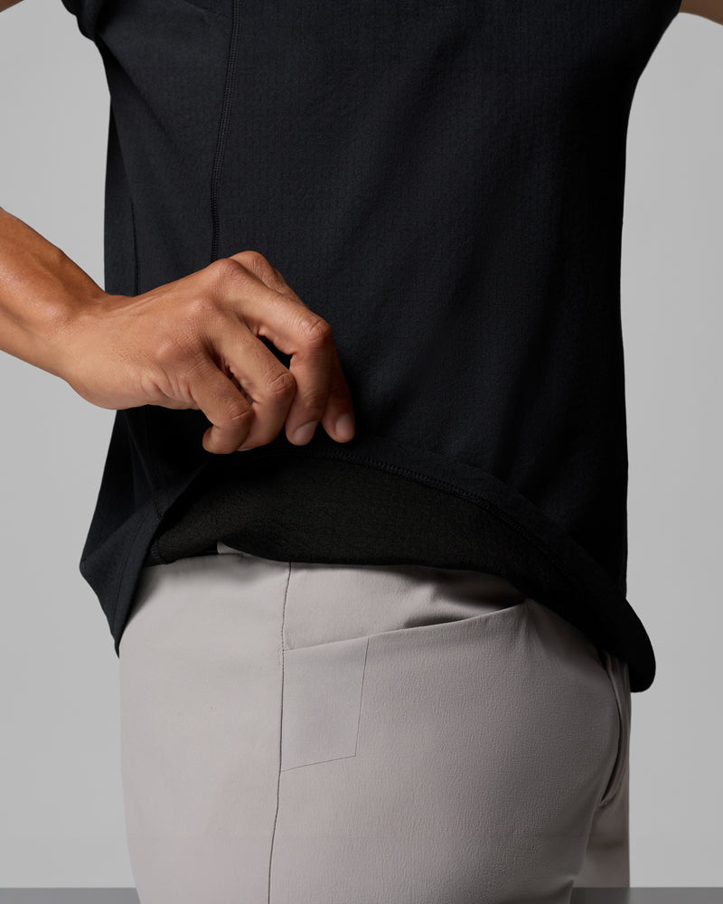 אדם מרים את שולי חולצת ה-Driventure Short Sleeve Shirt של קולומביה ישראל, וחושף שכבה נוספת שמתחתיה, בעודו לובש מכנסיים אפורים בהירים. התמונה מתמקדת בפלג הגוף העליון וביד.