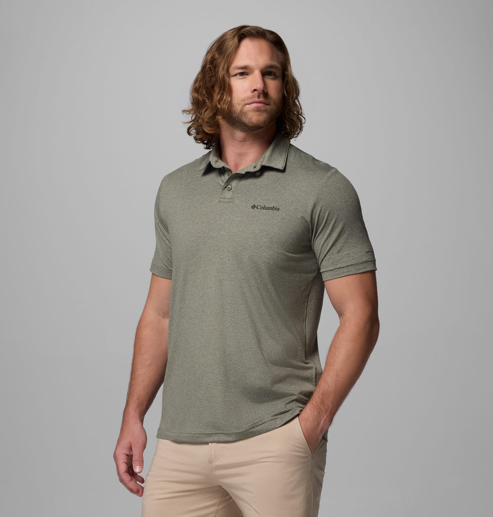 גבר בעל שיער ארוך וגלי לובש חולצת פולו "Parsons Point Polo M" בצבע אפור בהיר של קולומביה ישראל ומכנסיים בצבע בז', עומד כש יד אחת בכיסו על רקע אפור אחיד.