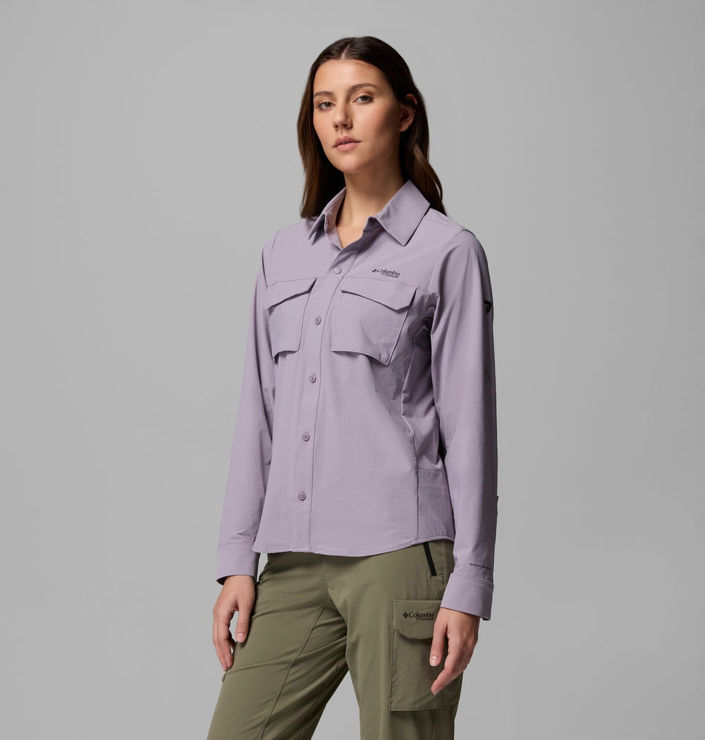 אישה עומדת פונה קדימה, לבושה בחולצת "Silver Ridge Elite Woven L/S" בצבע סגול בהיר מבית קולומביה ישראל, עם שני כיסים קדמיים, ומכנסי קרגו בצבע ירוק זית, כשהיא מצטלמת על רקע אפור אחיד.