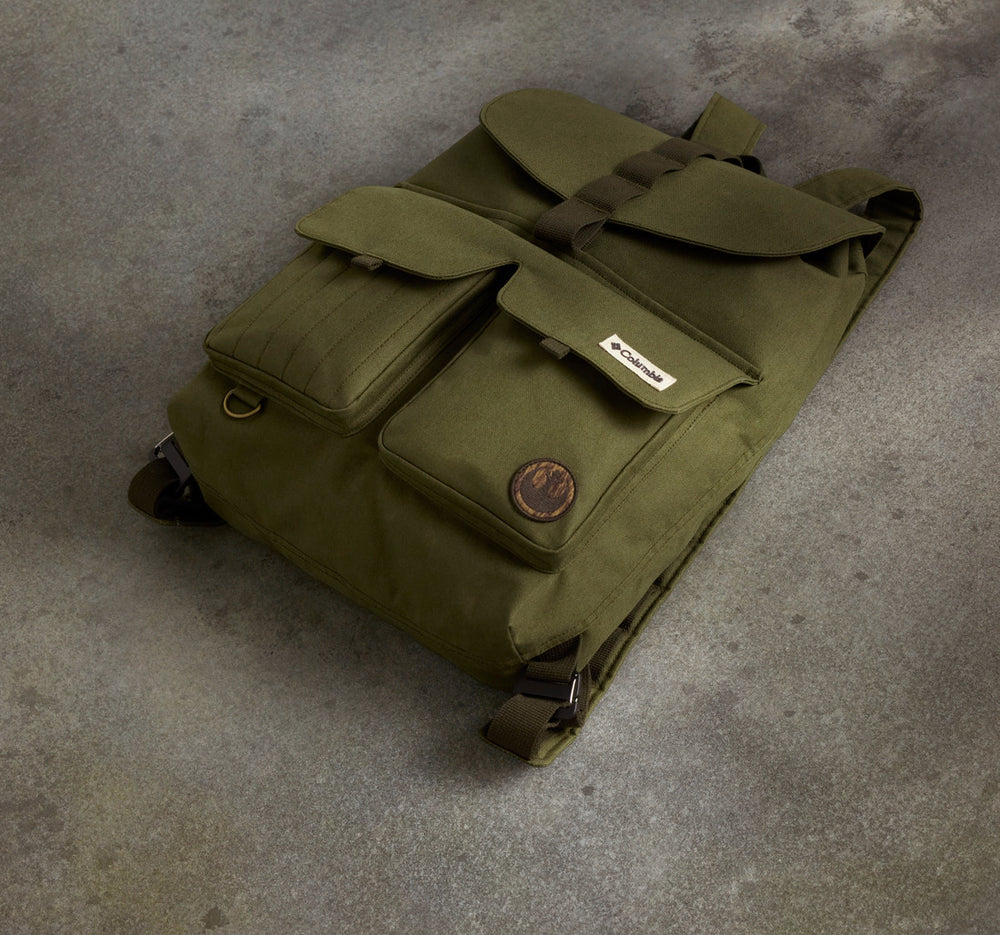תיק הגב "Endor Issue Cargo" של קולומביה ישראל בצבע ירוק זית כולל שני כיסים קדמיים, סגירות עם דש, רצועות חומות ותווית עגולה, והוא מוצג בשכיבה על משטח אפור בעל מרקם.